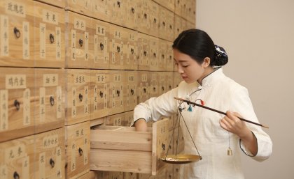 Woman looking through a drawer of Chinese medicine in a wall full of drawers